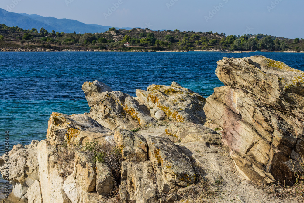 rocky tropic beach nature scenic landscape with stones on foreground and vivid blue sea lagoon water surface on background with view on island opposite coast in clear summer vacation weather time