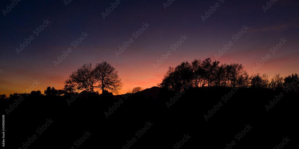 Aerial view of a spectacular sunset behind some beautiful mountains and the silhouette of some trees in the foreground.