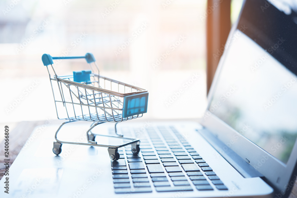 Online shopping concept. Shopping cart with laptop on the desk. - obrazy, fototapety, plakaty 