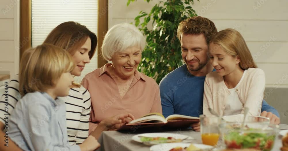 Portrait shot of the grandmother sitting with her family and grandchildren at the dinner table and they watching some book. Portrait shot of the grandmother sitting with her family and grandchildren at the dinner table and they watching some book.