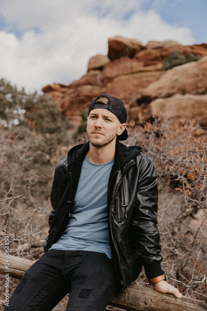Naklejka premium Portrait of Young Good Looking Casual Traveling Handsome Man Smiling Near Ancient Desert Red Rocks in Jacket Outside