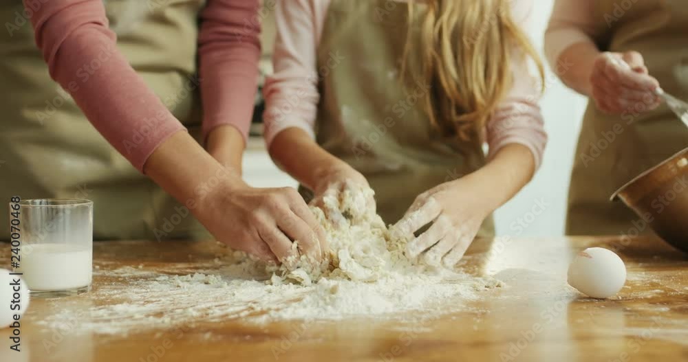 Camera zooming out from Caucasian female and kid's hands kneading a dough to the grandmother, mother and daughter cooking cookies together. Close up. Camera zooming out from Caucasian female and kid's hands kneading a dough to the grandmother, mother and daughter cooking cookies together. Close up.