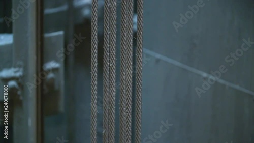 Closeup: Strong suspended cables inside elevator shaft move, carrying the car