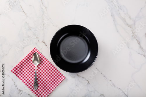 Black plate on marble countertop with red plaid napkin.