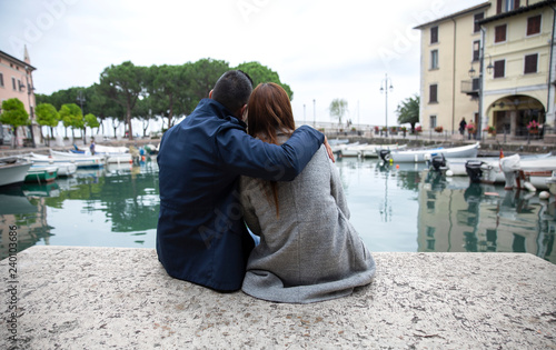 couple in love sitting on the waterfront. Couple in love on the shores of Lake Garda, Desenzano di Garda, Italy. In love couple on the waterfront. Couple hugging on a bench - Immagine