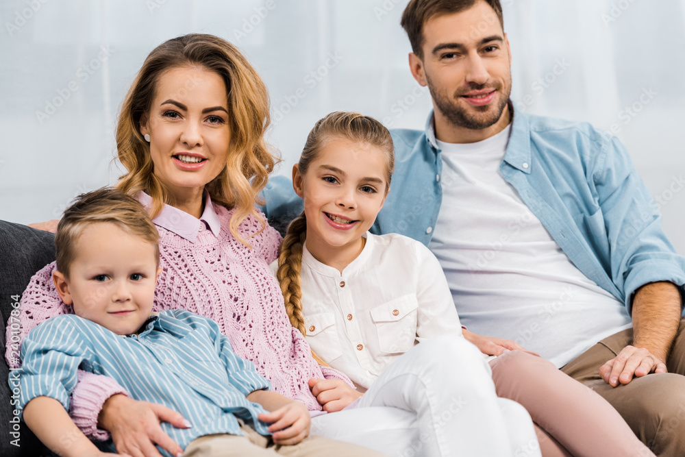 happy family sitting on sofa and looking at camera in apartment