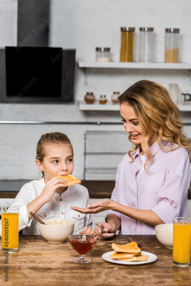 smiling mother looking at cute daughter eating toast with jam smiling mother looking at cute daughter eating toast with jam