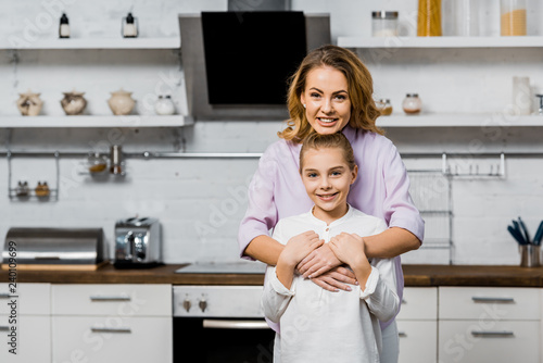 Cuadro en lienzo smiling woman embracing cute daughter and looking at camera in kitchen