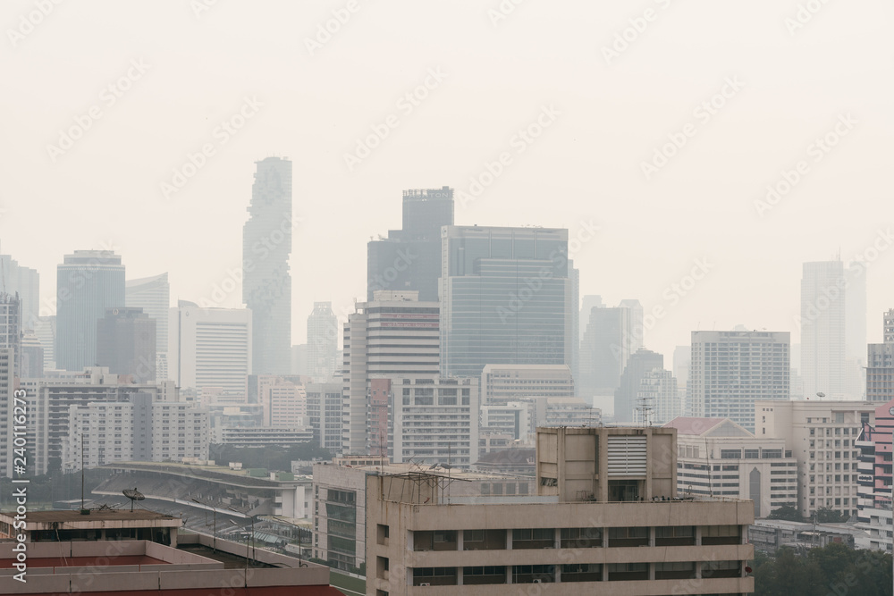 Obraz premium Air pollution effect made low visibility cityscape with haze and fog from dust in the air during sunset in Bangkok, Thailand. Image contain noise and grain.