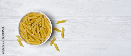 Italian raw penne rigate pasta on white wooden background