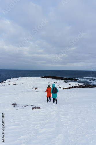 two girls in colorful and warm jackets stand on the snowy shore of the northern sea on a cold winter day in the Arctic Circle © Александр Коновалов