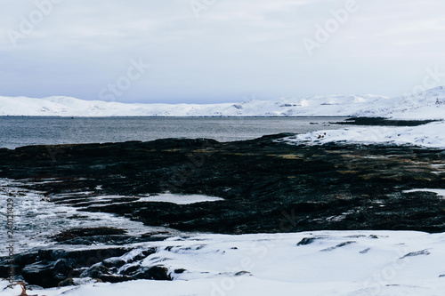 beautiful snow coast with sharp rocks and large stones of the cold blue sea in the north of the Arctic Circle