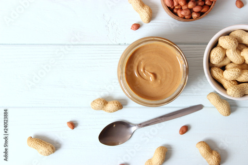  creamy peanut butter in a glass jar and peanuts beans on wooden background top view