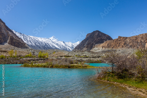 Panorama shot of small turquoise mountain lake under the sunny day with blue sky along Karakorum Highway in Passu, Hunza district of Pakistan.