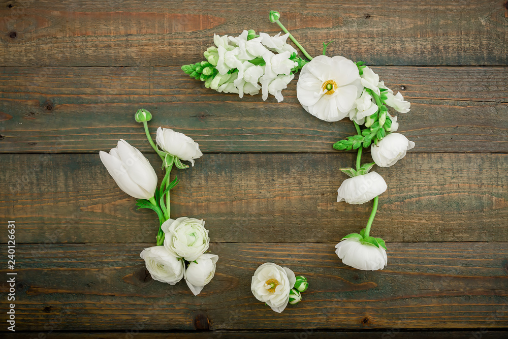Floral frame with white flowers and green leaves isolated on wooden background. Flat lay, top view