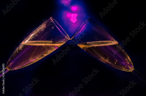 Two glasses of white wine for a couple toast to cerebrate Valentine’s Day with pink love shape bokeh light on black and blue background. photo