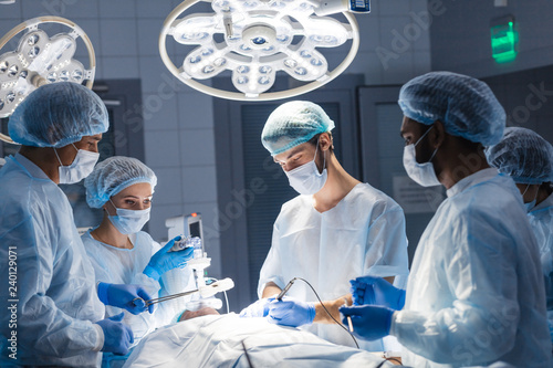 Urgent surgery. Professional smart intelligent surgeons standing near the patient and performing an operation while saving his life. Professional treatment and professional conduct concept.
