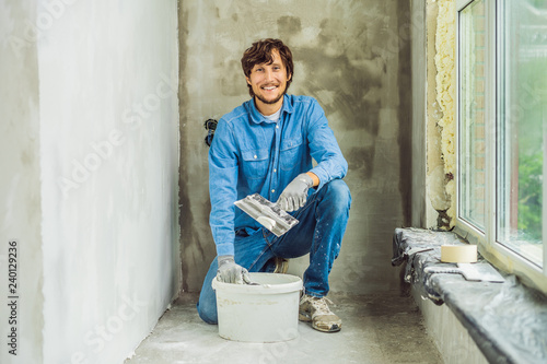 master is applying white putty on a wall and smearing by putty knife in a room of renovating house in daytime photo