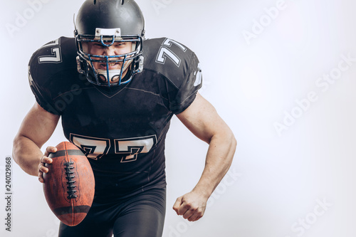 Isolated motion shot of American Football Quarterback player in professional protective black uniform and helmet passing a ball over white background.