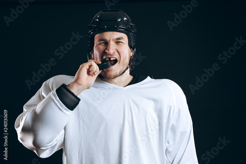 Caucasian Hockey player tastes the puck, having fun, demonstrates the way he lost the tooth, looking at camera isolated on black background.