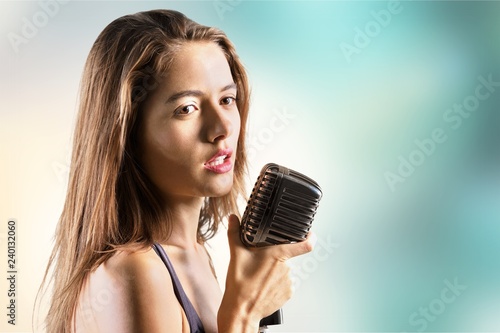 Young woman singing with microphone on blurred background