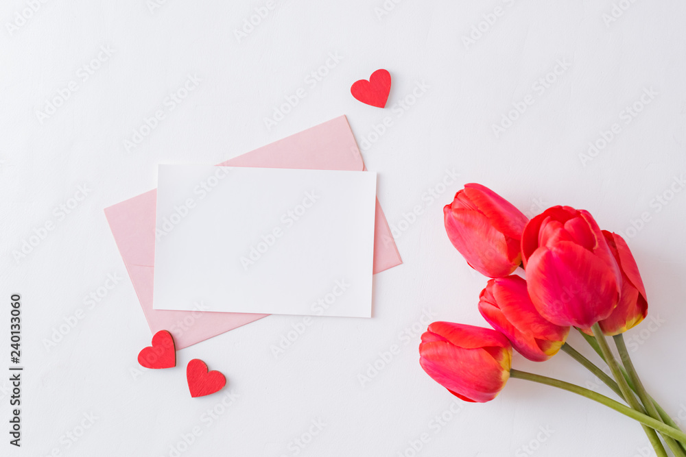 Mockup white greeting card, red hearts and envelope with red tulips on a light background Mockup white greeting card, red hearts and envelope with red tulips on a light background