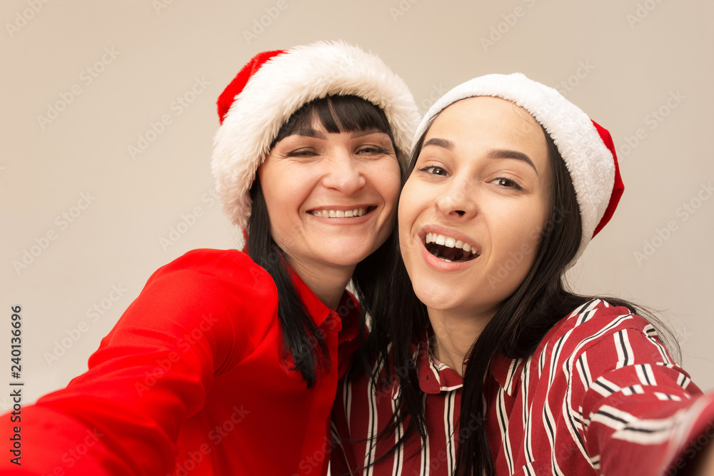 A portrait of a happy mother and daughter in Santa hat at studio on gray background. Human positive emotions and facial expressions concept A portrait of a happy mother and daughter in Santa hat at studio on gray background. Human positive emotions and facial expressions concept