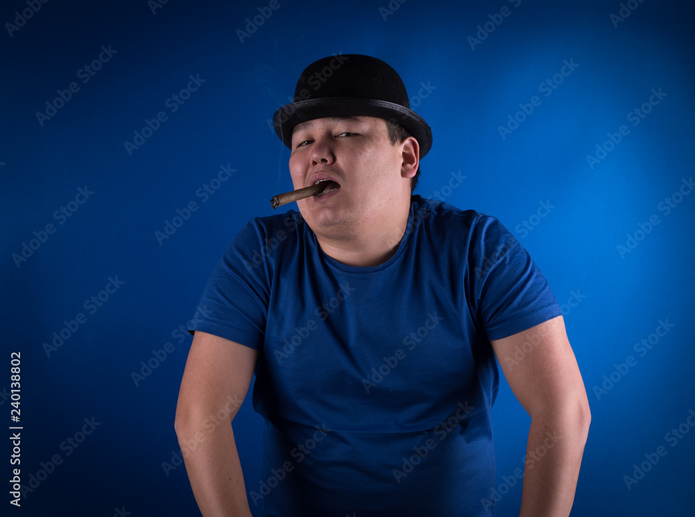studio portrait of a man with a cigar in a hat on a blue background studio portrait of a man with a cigar in a hat on a blue background