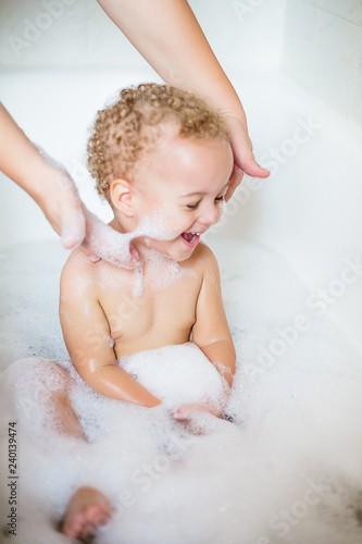 Cute two year old boy taking a relaxing bath with foam
