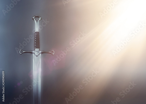 mysterious and magical photo of silver sword over black background with golden light rays. Medieval period concept.