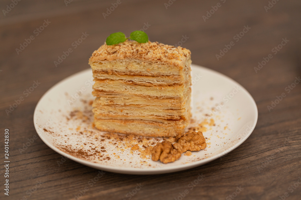 Piece of cake Napoleon on white plate on wooden background. Russian cuisine, layered cake with cream, close up view. Selective focus.