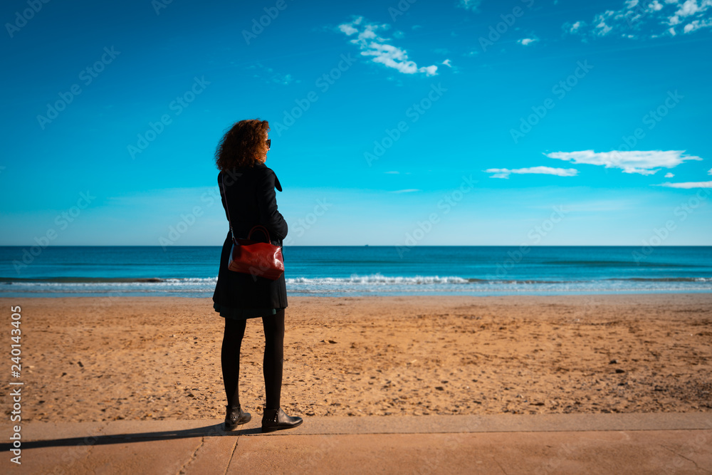 Women wearing autum or winter clothes looking at the sea on a sunny day . Orange and teal look with Copy space. Women wearing autum or winter clothes looking at the sea on a sunny day . Orange and teal look with Copy space.