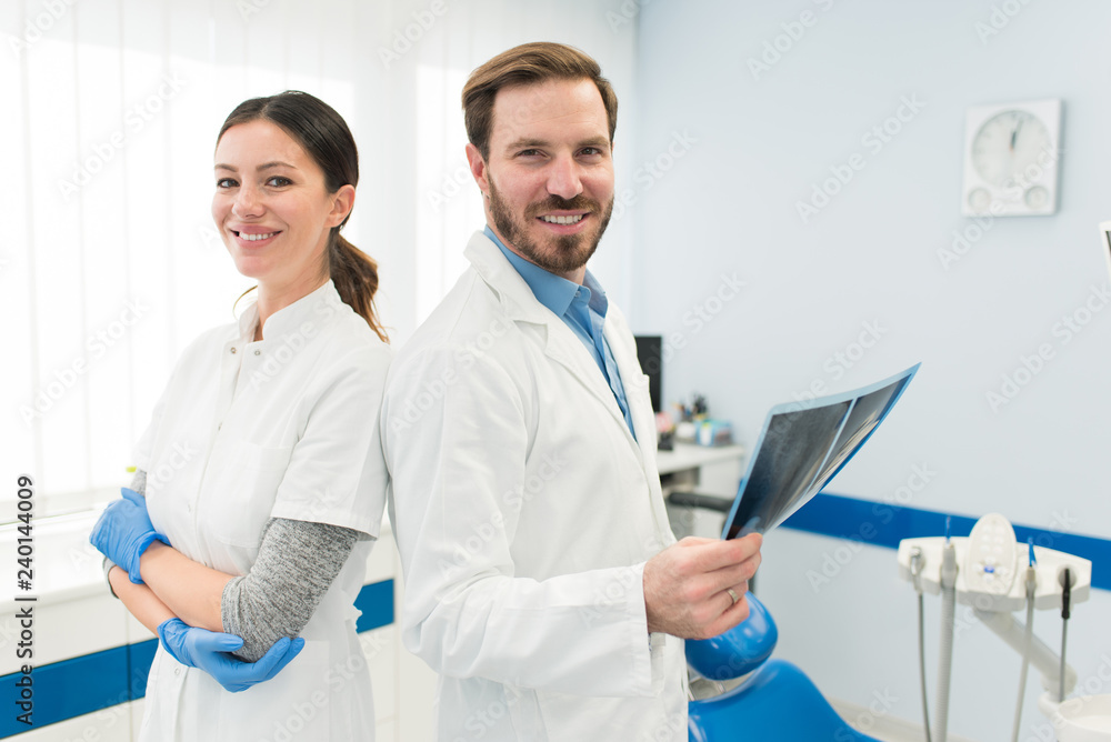 Fototapeta premium Portrait of two young attractive female and male doctor looking at camera holding a x-ray screening working in modern clinic. Successful young doctors concept.