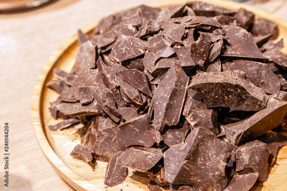 Close-up of a pile of pieces of natural dark chocolate on a round wooden plate. Concept diet, healthy food, lowcalorie dessert, carob