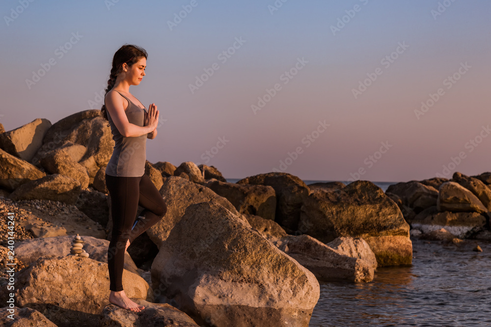 young girl doing yoga standing in the pose of a tree on the rocks on the background of the sea young girl doing yoga standing in the pose of a tree on the rocks on the background of the sea