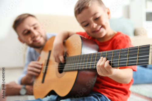 Father teaching his little son to play guitar at home
