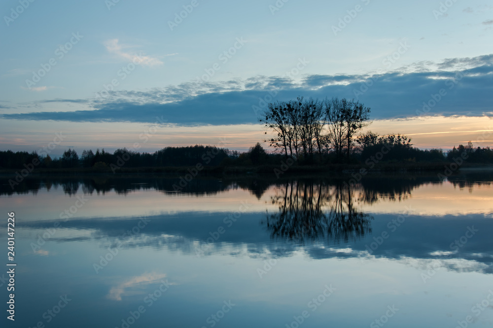 Gray cloud and trees on the shore reflecting in the lake