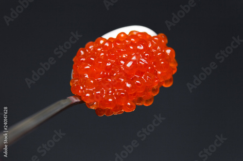 Closeup macro metal long spoon with slide red salmon caviar on black background. Top view. Concept gourmet snack seafood appetizer