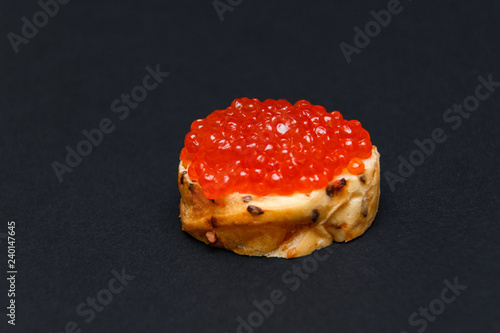 Closeup tasty canape with slide of red salmon caviar on white grained bread on black background. Concept gourmet snack healthy sandwich with baguette, seafood appetizer photo