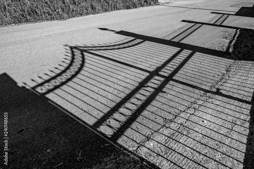 Shadow of beautiful wrought iron garden fence on dusty public road in spring afternoon in Corfu, Greece. Black and white travel image