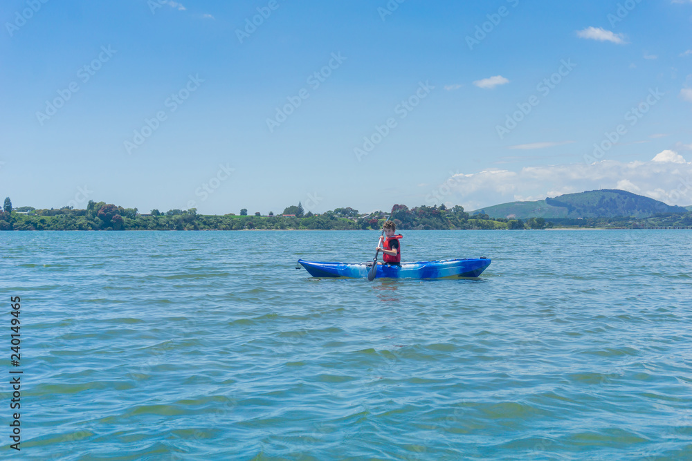 Young boy paddling blue and white kayak in harbour.
