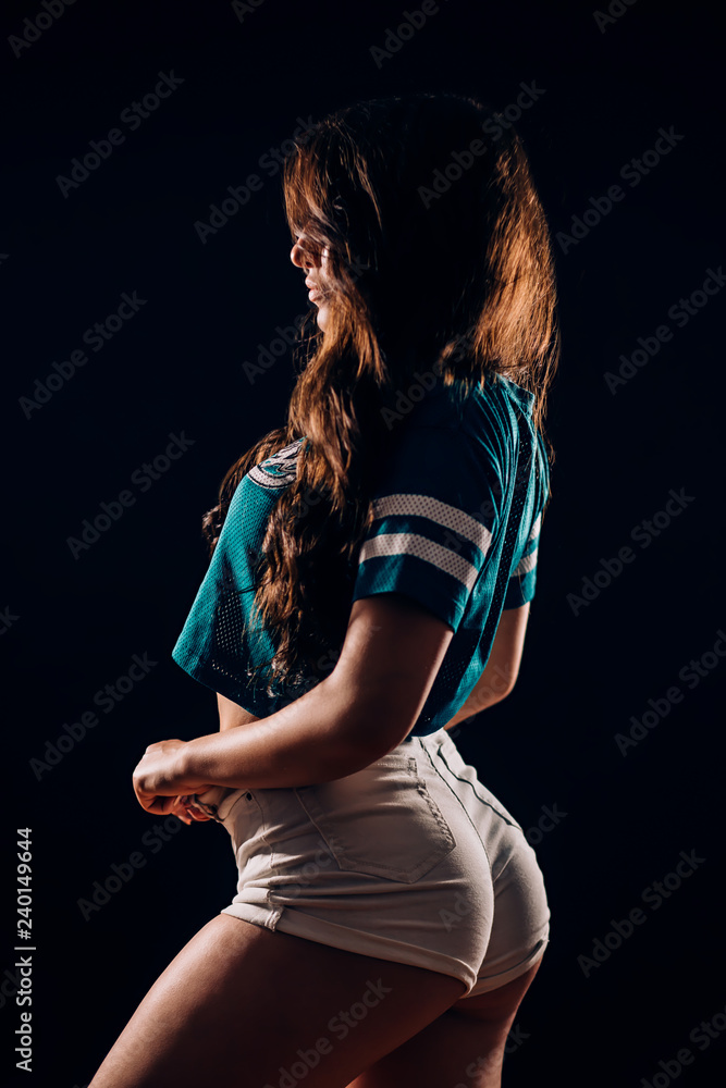Sideways sexy portrait of young hot brunette woman in short white shorts  and t-shirt in dark on black background, silhouette fitness dancer girl  Stock Photo | Adobe Stock
