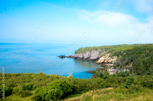 Scenic coastal view. Fog over the ocean in the distance. Blue ocean and sky. Trees and cliff. Taken at Cape Spencer, NB, Canada.