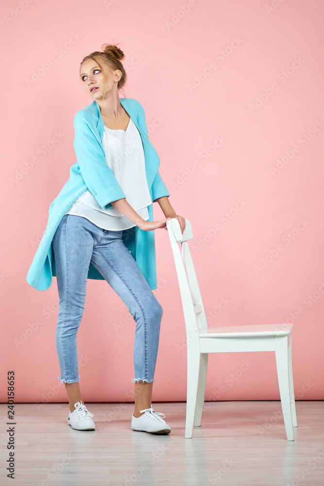 happy young girl model posing in studio on a pink background in spring clothes. fashion for teens, bright colors. turquoise coat