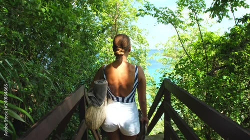 Girl carrying beach towel walking on a deck platform with jungle and ocean