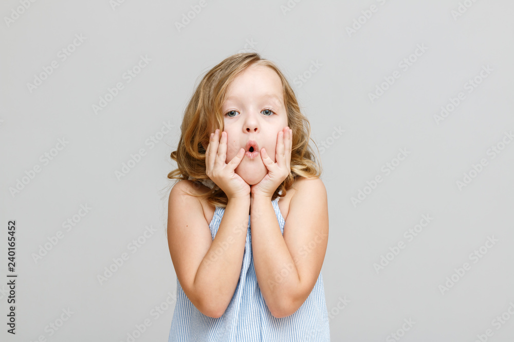 Portrait of a little girl on a gray background. The child is looking straight at the camera with surprise.