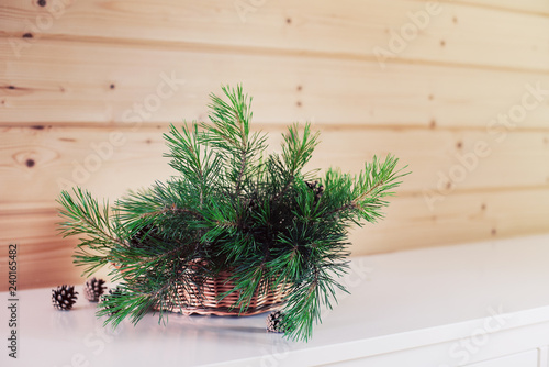 Green pine branches in a wicker basket on a white chest of drawers on a wooden background