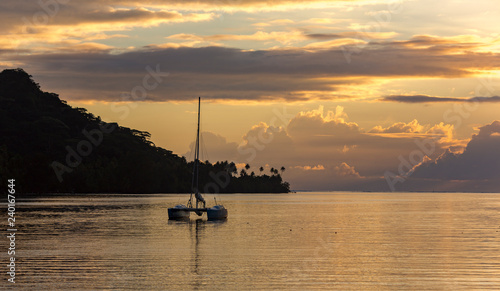 Lonely catamaran against the background a golden sunset near Bora-Bora island in the Pacific ocean, French Polynesia.
