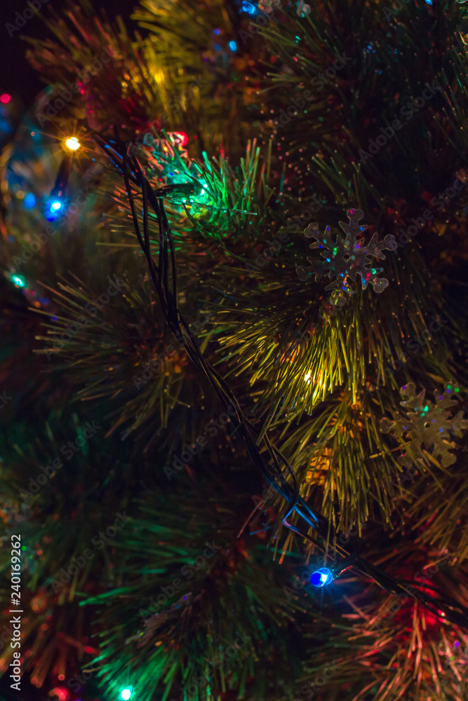 Christmas tree on with snowflakes and garland with dark green, blue, red and yellow lights on right side of frame Christmas tree on with snowflakes and garland with dark green, blue, red and yellow lights on right side of frame