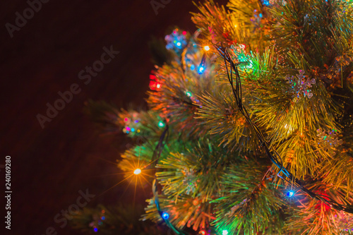 Christmas tree part with snowflakes and garland with green  blue  red and yellow lights on right side of frame and brown background